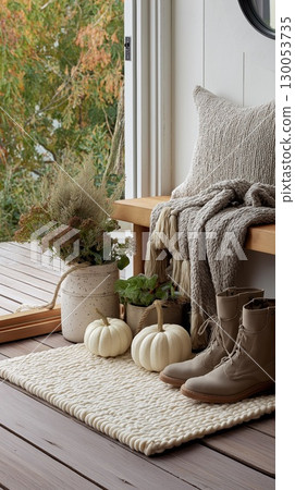 Cozy autumn porch corner with neutral-toned decor, white pumpkins, boots, and soft textured fabrics 130053735