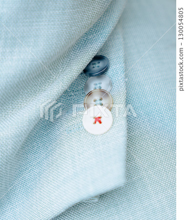 Macro shot of a light blue textured jacket sleeve with four decorative buttons. One of the buttons has red stitching detail, creating a stylish and unique fashion accent. Perfect for illustrating Macro shot of a light blue textured jacket sleeve with four decorative buttons. One of the buttons has red stitching detail, creating a stylish and unique fashion accent. Perfect for illustrating 130054805