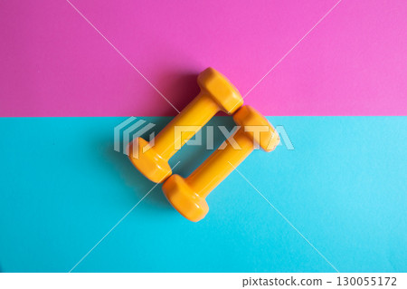 Two orange dumbbells on a pink and blue background with copy space. A tool for training, sport and activity in summer time. Two orange dumbbells on a pink and blue background with copy space. A tool for training, sport and activity in summer time. 130055172