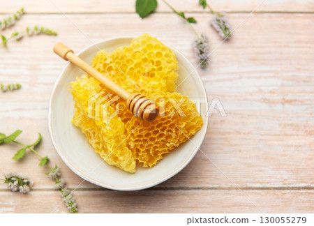 Honeycomb in bowl with honey dipper and fresh mint on wooden table Honeycomb in bowl with honey dipper and fresh mint on wooden table 130055279