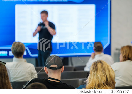 Audience listens to speaker at seminar with screen in background 130055507