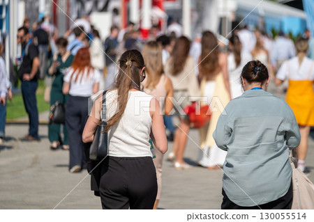 Crowd of people walking through outdoor event during sunny day 130055514