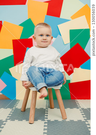 A cheerful child is happily sitting on a small chair, creating a delightful scene against a vibrant and colorful background that enhances the overall positivity and joy of the moment 130056039