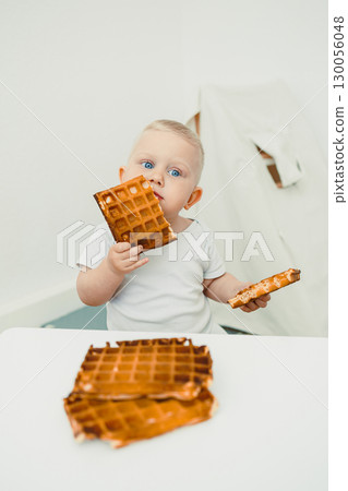 A Happy Child Enjoying Delicious Waffles An Adorable Toddler Biting into a Sweet Snack in a Joyful Moment During Breakfast Time, Radiating Delight and Fun with Every Bite of Their Treat 130056048