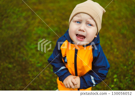 An adorable child, dressed in a bright rain jacket and a cozy beanie, conveys a wide range of emotions while joyfully exploring the wonders of nature all around them, from smiles to laughter 130056052