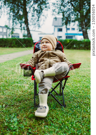 On this cozy day, a charming young kid relaxes in a garden chair, stylishly dressed in a fun outfit and playful footwear, enhancing their joyful and playful vibe with each passing moment On this cozy day, a charming young kid relaxes in a garden chair, stylishly dressed in a fun outfit and playful footwear, enhancing their joyful and playful vibe with each passing moment 130056054
