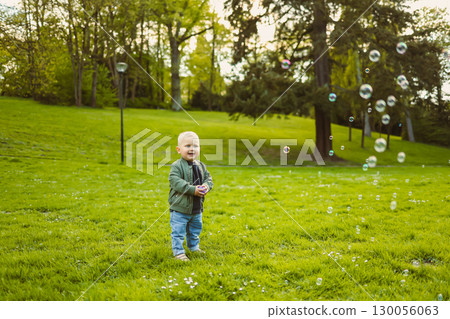Little 2 year old boy running on green grass with soap bubbles. Toddler boy enjoying a walk in nature. Child having fun in city park. Little 2 year old boy running on green grass with soap bubbles. Toddler boy enjoying a walk in nature. Child having fun in city park. 130056063