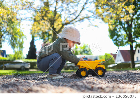 Toddler boy playing on the playground outside with his plastic car. Cute 2 year old boy playing with a car in the yard. Child walking outdoors. Toddler boy playing on the playground outside with his plastic car. Cute 2 year old boy playing with a car in the yard. Child walking outdoors. 130056073