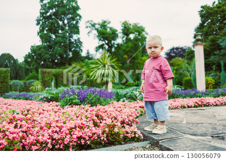 A charming toddler joyfully playing and exploring in a lush garden setting, surrounded by an array of colorful, blooming flowers that create a beautiful and vibrant outdoor environment 130056079