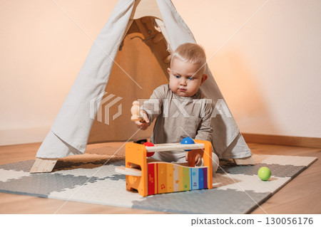 A playful baby is deeply engaged and having fun with a colorful musical toy while inside a cozy and comfortable tent, creating an enchanting environment filled with joy and creativity during playtime 130056176