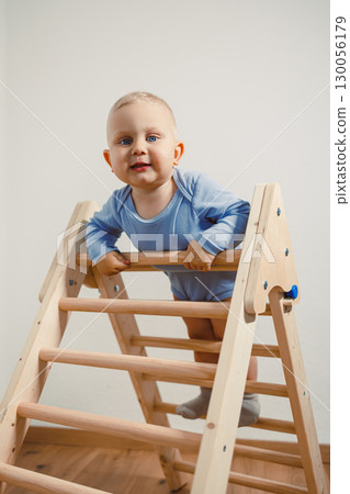 An adorable baby joyfully climbing on a wooden play ladder a delightful and safe way to foster fun activities that contribute to the essential early childhood development of your little one 130056179