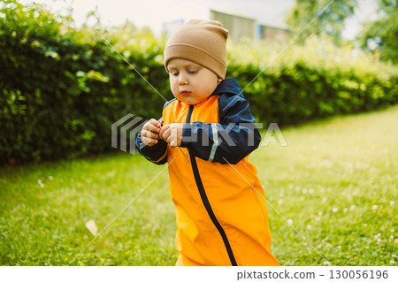 An adorable child, donned in vibrant rain gear, joyfully playing outdoors in the park, surrounded by greenery and the happiness of childhood, fully embracing the adventurous spirit of life 130056196