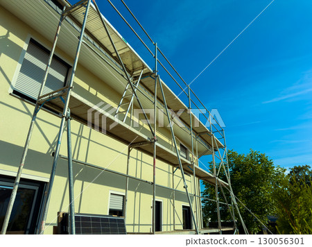 The temporary scaffolding on the large building undergoing renovation contrasts with the bright blue sky, highlighting the dynamic architecture and ongoing construction activities below 130056301