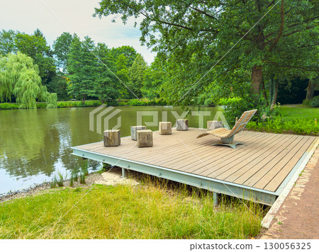 Discover a truly tranquil lakeside retreat featuring a charming wooden dock and inviting seating area, all nestled amid lush greenery, perfectly set in a serene and picturesque natural landscape Discover a truly tranquil lakeside retreat featuring a charming wooden dock and inviting seating area, all nestled amid lush greenery, perfectly set in a serene and picturesque natural landscape 130056325