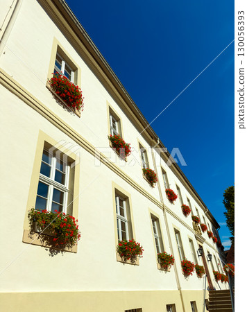 The charming architectural facade is adorned with beautiful flower boxes, gracefully positioned underneath a clear, vibrant blue sky, enhancing the entire scene, creating an inviting atmosphere The charming architectural facade is adorned with beautiful flower boxes, gracefully positioned underneath a clear, vibrant blue sky, enhancing the entire scene, creating an inviting atmosphere 130056393