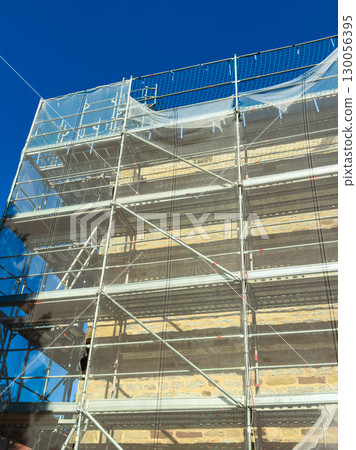 The scaffolding against the blue sky highlights safety and ongoing construction progress, showcasing the hard work and dedication involved in transforming our cities through urban development 130056395