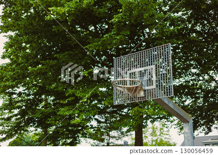 An outdoor park setting featuring a basketball hoop, elegantly surrounded by a plethora of lush green trees, inviting individuals of all ages to partake in this dynamic activity and enjoy the day An outdoor park setting featuring a basketball hoop, elegantly surrounded by a plethora of lush green trees, inviting individuals of all ages to partake in this dynamic activity and enjoy the day 130056459