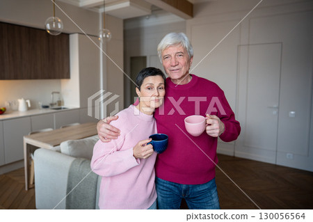 Calm retired wife and husband embracing in morning while drinking tea coffee looking at camera 130056564