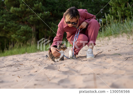 Woman strolls along beach soothing anxious scared cat, making comfort support for pet on walk 130056566