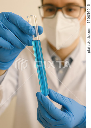 Scientist wearing blue gloves holding glass test tube with blue liquid for laboratory research and chemical analysis 130056946
