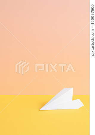 Paper airplane on yellow surface with peach background, symbolizing creativity and imagination in bright, minimalistic setting 130057600