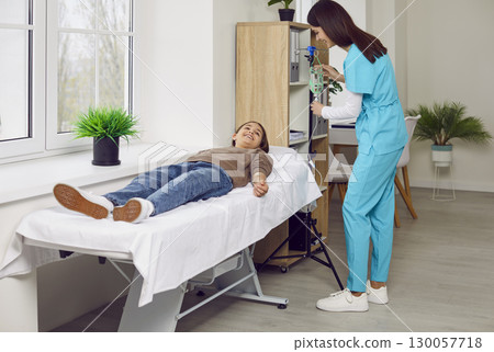 Smiling nurse gives intravenous medical infusion to happy child patient at clinic 130057718