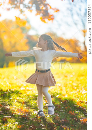 Little girl playing and having fun in autumn park surrounded by colorful leaves, joyful carefree childhood moment in nature during fall season 130057864