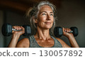 A confident senior woman lifting dumbbells during a strength training workout 130057892