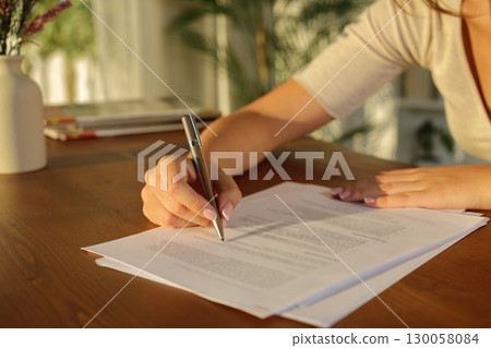 Woman hand filling document on wooden table at sunset 130058084