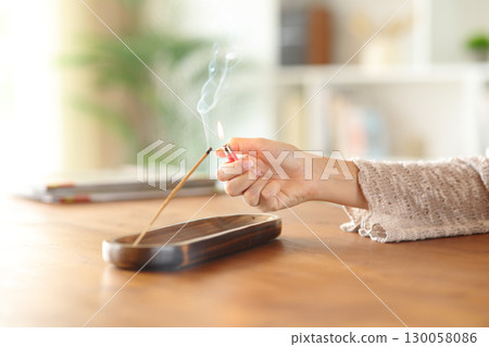 Woman hand lighting incense stick with a lighter at home Woman hand lighting incense stick with a lighter at home 130058086