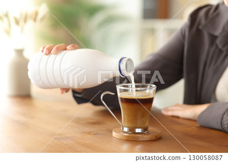 Woman hand pouring milk from bottle in coffee cup 130058087