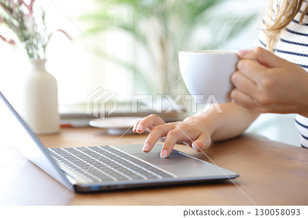 Woman hands drinking coffee using personal computer 130058093