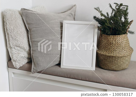 White blank wooden frame mockup. Christmas spruce tree branches in basket. Linen and teddy cushions on beige bench. Poster product display. Scandinavian festive winter home decor, nordic design. 130058317