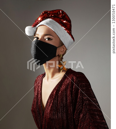 Woman with red christmas hat, black medical mask. Fashion shiny style for xmas time. Protection from flu on holidays Woman with red christmas hat, black medical mask. Fashion shiny style for xmas time. Protection from flu on holidays 130058471
