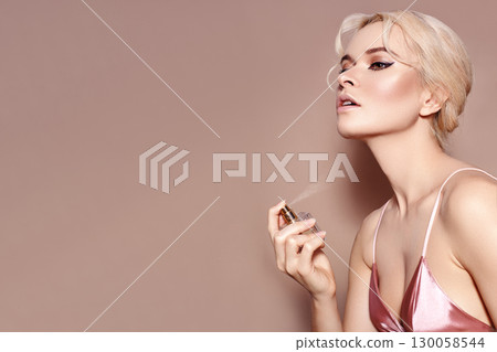 Beautiful Woman Applying Perfume Spray on neck. Blond Model with sexy Retro Make-up in Pink Lingerie Smells Fragrance 130058544