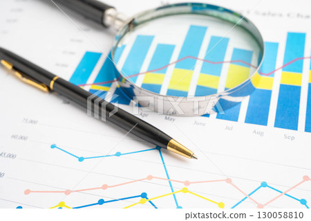 Magnifying glass on data business graphs paper. Magnifying glass on data business graphs paper. 130058810