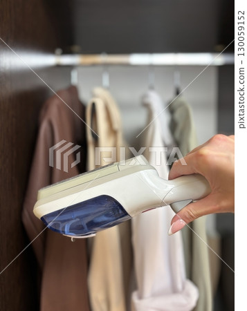 Woman using steam iron for clothing care in wardrobe at home. Female ironing garments, household chores, laundry and closet organization concept 130059152