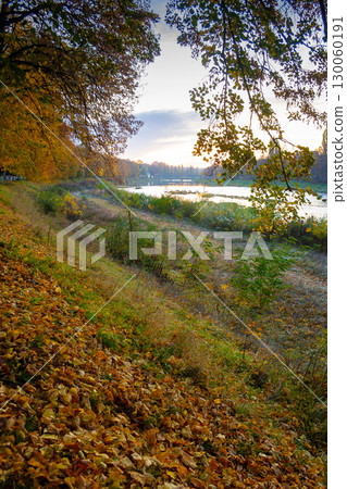 uzhhorod, ukraine - 31 oct, 2009: river uzh at dawn in autumn. beautiful cityscape scenery in morning light. scenic linden alley in fall colors. fallen foliage on the ground uzhhorod, ukraine - 31 oct, 2009: river uzh at dawn in autumn. beautiful cityscape scenery in morning light. scenic linden alley in fall colors. fallen foliage on the ground 130060191