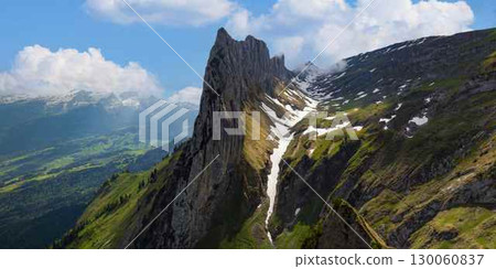 Stunning rocky peak rises above lush green valleys under a bright sky in the Swiss Alps during summer 130060837