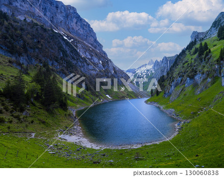 Mountain lake surrounded by green hills and majestic peaks on a sunny day in a tranquil natural setting 130060838