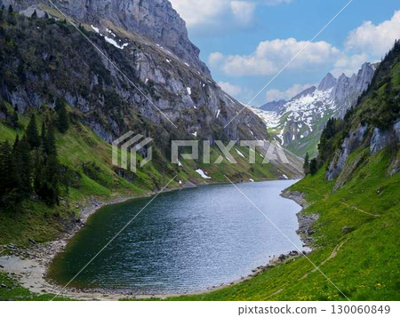 Scenic mountain landscape with a tranquil lake surrounded by lush greenery and snow-capped peaks 130060849
