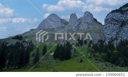 Scenic mountain landscape with towering peaks and lush greenery under a blue sky filled with fluffy clouds 130060852