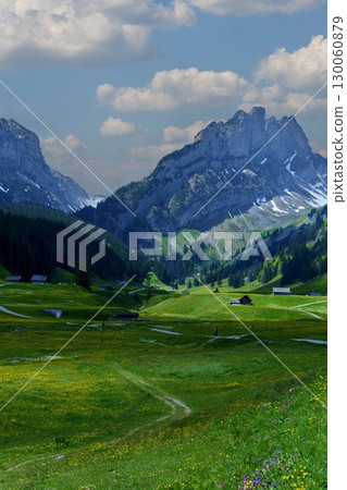 Majestic mountains tower over lush green valleys and charming settlements in a picturesque landscape during daytime 130060879