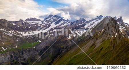 Panoramic view of snow-capped mountains under a cloudy sky with green valleys in springtime 130060882