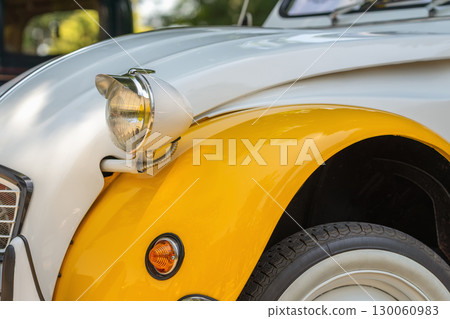 Headlamp and wing Citroen. Close-up of classic Citroen 2CV headlight and yellow fender with iconic rounded design. Concept of vintage car styling, retro auto details, collectible vehicle charm 130060983