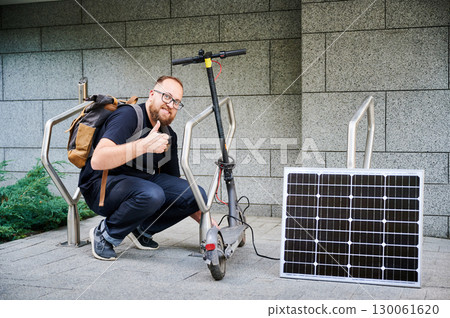 Man connects solar panel to electric scooter for charge, giving thumbs up. Integration of solar power as sustainable energy source for charging electric scooters, promoting eco-friendly transportation Man connects solar panel to electric scooter for charge, giving thumbs up. Integration of solar power as sustainable energy source for charging electric scooters, promoting eco-friendly transportation 130061620
