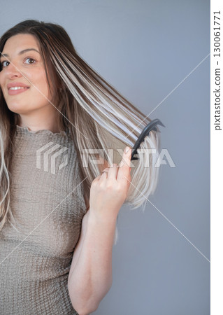 Young woman caring for hair extensions using soft wide tooth comb for easy gentle combing in beauty salon 130061771