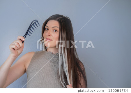 Beautiful long hair extensions young woman using special comb for gentle hair care in professional beauty salon 130061784