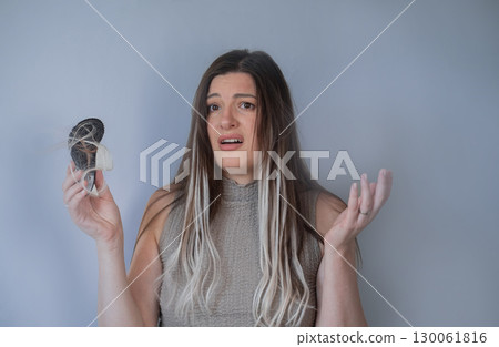 Worried woman looking at hairbrush full of strands concerned about hair loss and thinning hair problem 130061816