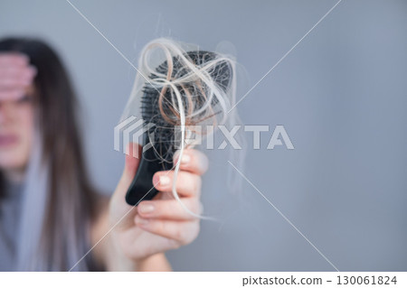 Hairbrush full of strands in young womans hands showing hair breakage and hair loss problem 130061824